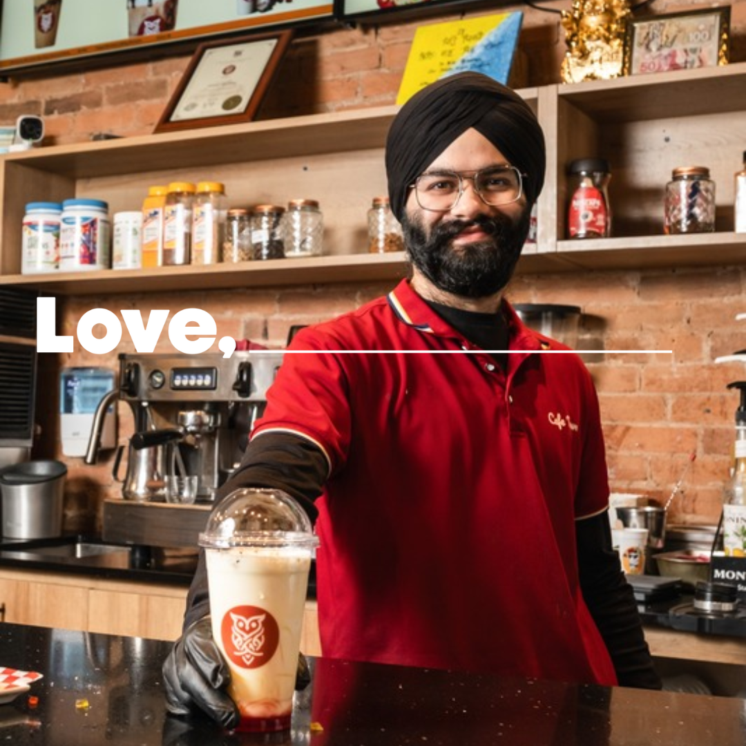 A man stands behind a cafe counter, holding an iced coffee.